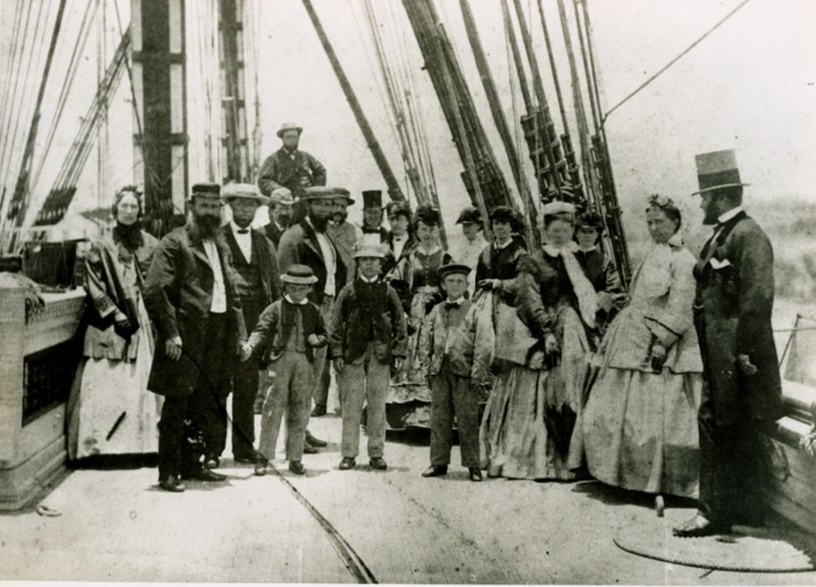 black and white photo of men and women gathered on the deck of a sailing ship