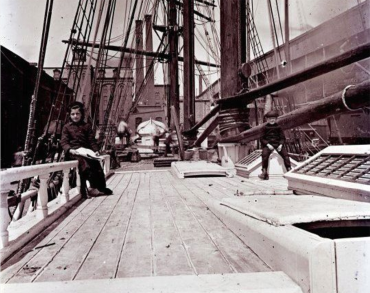 historic photograph of a boy and a girl sitting on the deck of a large sailing vessell